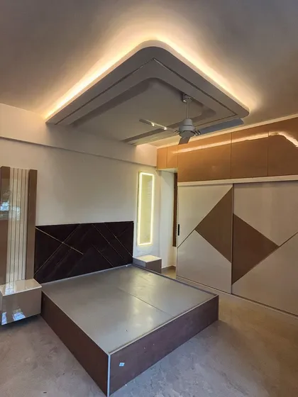 A beautiful room designed and executed by our team. The space features a sliding wardrobe with a patterned design that complements the dark wood headboard and elegant false ceiling.