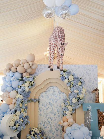 A whimsical baby shower entrance with a giraffe prop, a balloon arch, and custom-printed wallpaper.