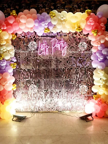 A "Let's Party" photo booth with a shimmering sequin wall and a colorful pastel balloon frame. The neon sign adds a fun and modern element, perfect for capturing memories.