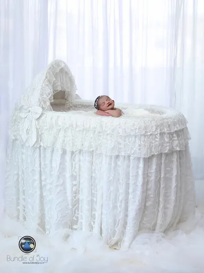 A wide-angle shot of a newborn yawning in an elegant, oversized white lace bassinet, creating a dramatic and angelic portrait.
