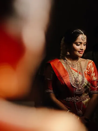 An artistic bridal portrait, with the bride's face softly lit against a dark background. The foreground blur adds depth and a sense of intimacy to the shot.