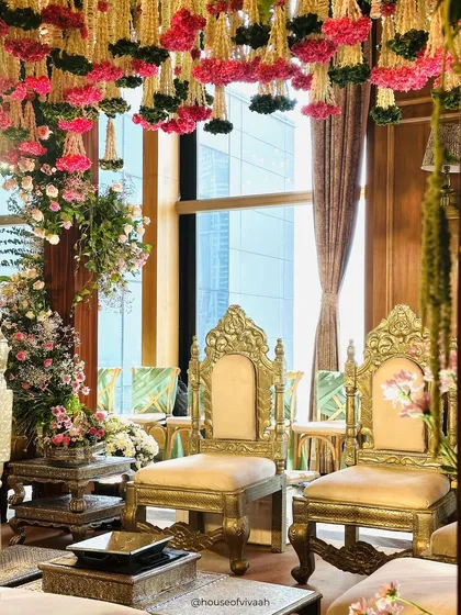 The ornate golden chairs for the bride and groom, set against a backdrop of hanging floral strings, capturing the regal and intimate details of the ceremony space.