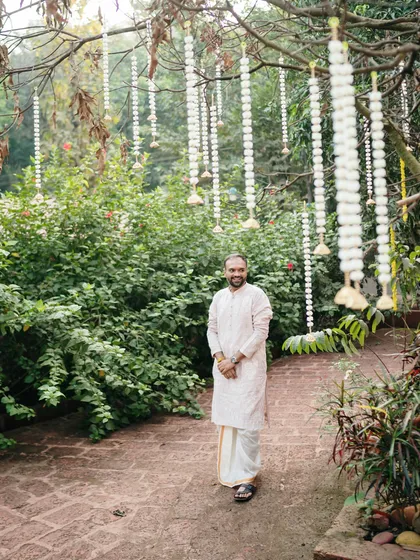 The groom standing in a beautifully decorated garden. This environmental portrait captures him in the midst of the wedding setting, looking happy and serene.