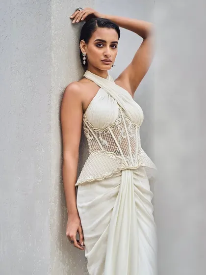 Sculpted silk frames strength in softness. This ivory gown features a structured halter-neck corset with a peplum detail, paired with a draped skirt that flows with a quiet, modern romance.