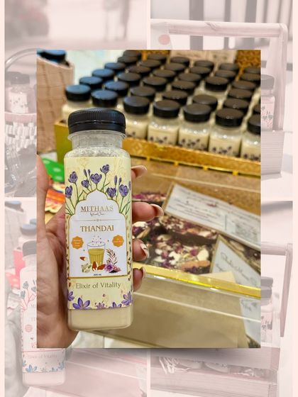 Holding up a bottle of my Thandai, the "Elixir of Vitality". In the background, you can see them being prepared for a large festive order, ready to bring joy to many.