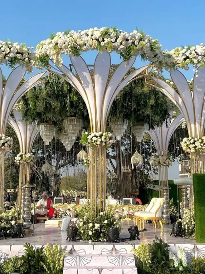 This unique mandap design features towering, stylized floral structures that resemble blooming lotuses. The combination of white fabric, gold frames, and fresh flowers creates a modern yet regal look for a memorable wedding ceremony.