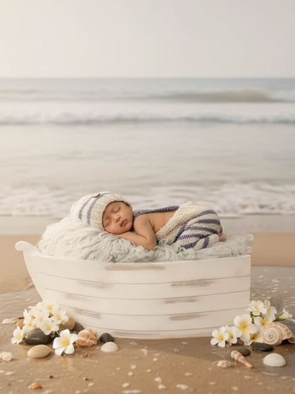 A unique composite photo showing a newborn sleeping in a boat prop on a sandy beach with gentle waves in the background.