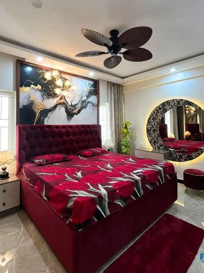 A luxurious bedroom with a bold red velvet bed, a large abstract art piece, and a stunning backlit circular vanity mirror.