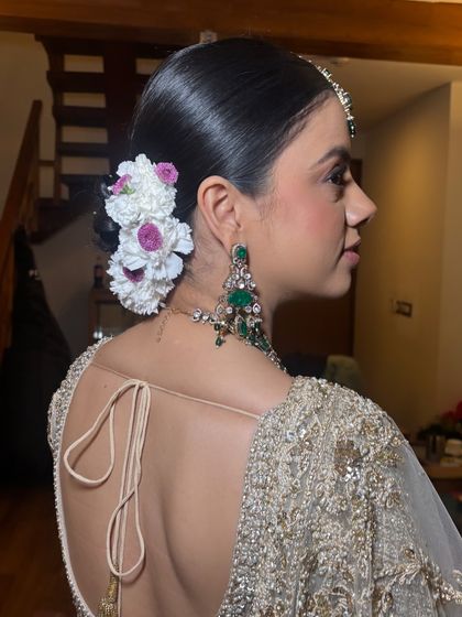 A side profile showcasing the sleek finish of the bridal bun. The flowers are placed strategically to enhance the style without overwhelming it, creating a very balanced and elegant look.