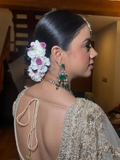 A side profile showcasing the sleek finish of the bridal bun. The flowers are placed strategically to enhance the style without overwhelming it, creating a very balanced and elegant look.
