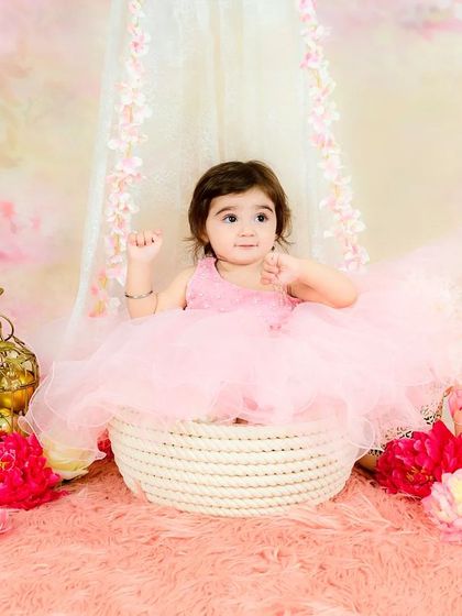 A baby girl in a pink tutu sits in a basket surrounded by flowers, looking up with a sweet expression. A truly enchanting portrait.