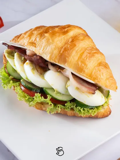 Our Bacon and Egg Croissant Sandwich. A flaky, buttery croissant filled with crispy bacon, sliced boiled eggs, fresh lettuce, and tomato for a hearty and delicious breakfast or lunch.