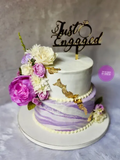 This two-tiered engagement cake features a lovely lavender marble effect on the bottom tier. Complemented by purple and white flowers and a "Just Engaged" topper, it's a sophisticated choice for a special announcement.