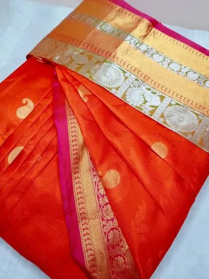An orange and pink silk saree with a silver and gold border.