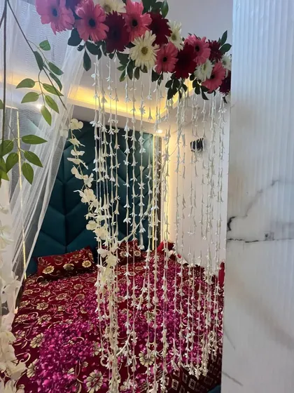 A romantic wedding night room decoration, showing a bed canopy adorned with fresh gerbera daisies and hanging strings of jasmine flowers.
