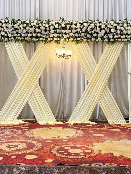 We designed this elegant and modern stage for a Beegara Oota. The clean white drapes, classic floral arrangements, and a central chandelier provide a sophisticated backdrop for post-wedding events.