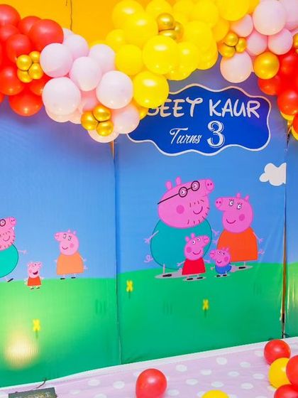 A cheerful Peppa Pig-themed backdrop, framed by a red, yellow, and pink balloon arch.