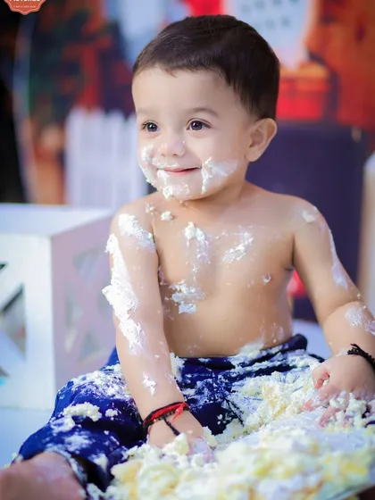 A close-up of the birthday boy, covered in cake and smiling from ear to ear. This shot captures the pure, messy joy of a cake smash.
