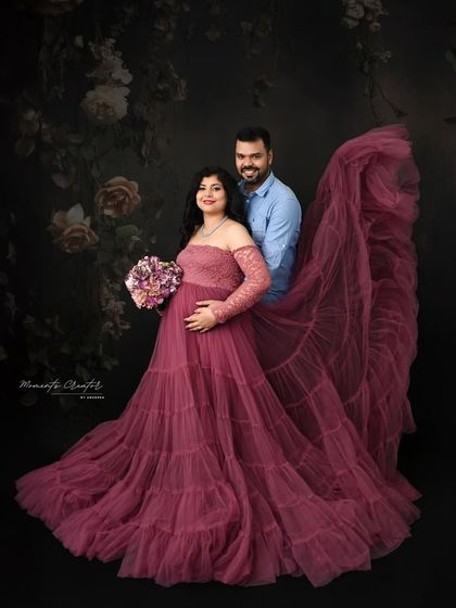 A powerful couple's portrait featuring a dramatic fabric toss. The flowing mauve gown adds a sense of movement and grandeur to this artistic shot against a dark floral backdrop.