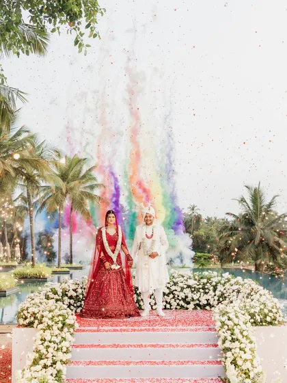 A picture-perfect moment from a Goa wedding, with rainbow smoke bombs creating a colorful backdrop for the couple's Varmala.