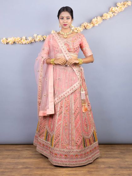 A full-length view of the elegant pastel peach lehenga. The skirt is heavily embellished with geometric and floral embroidery, with a pop of color at the border.
