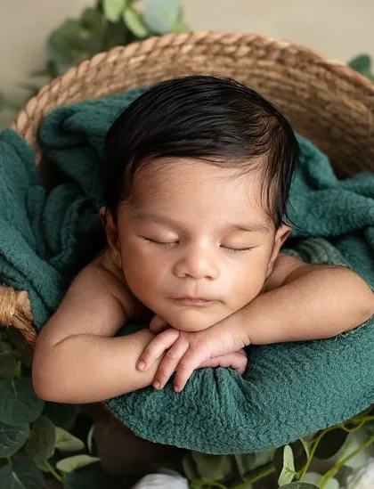 The classic chin-on-hands pose, with a newborn nestled in a basket surrounded by eucalyptus leaves. This pose highlights their adorable, sleepy features in a natural setting.