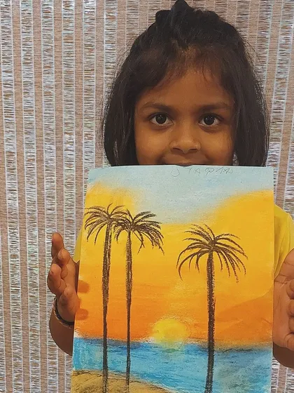 A student proudly shows her soft pastel drawing of a beach sunset, featuring lovely blending of colors.