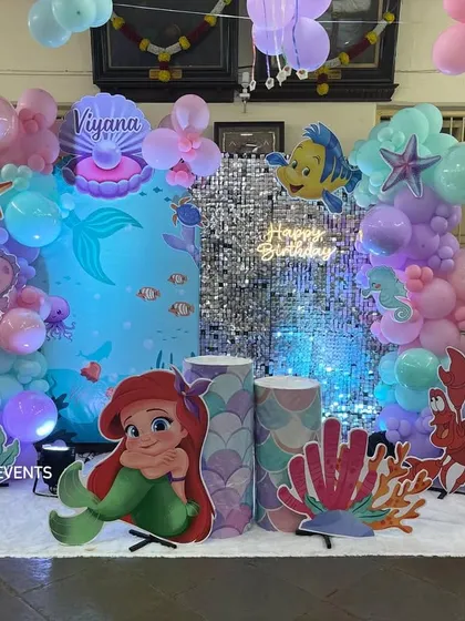 For kids' parties, I bring their favorite stories to life. This 'Under the Sea' birthday party features a complete setup with a Little Mermaid theme, including character cutouts, a shimmer backdrop, themed props, and a custom balloon arrangement in pastel colors.