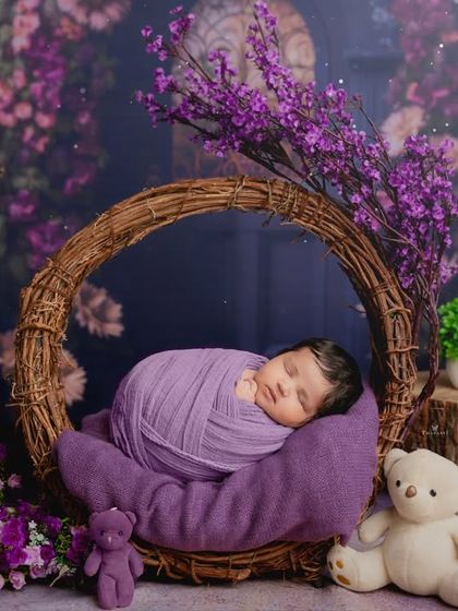 A wider view of the purple-themed newborn setup, featuring a wreath of vines, teddy bears, and floral arrangements that create a lush, dreamy atmosphere.