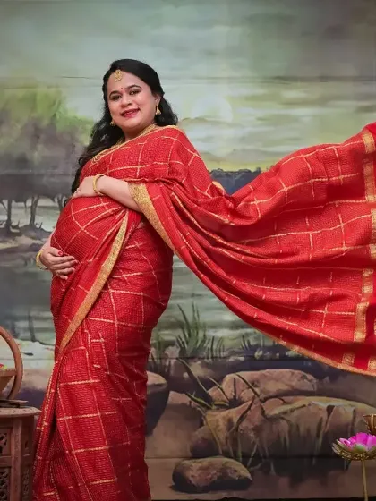 The flowing fabric of the saree creates a sense of movement and grace in this stunning solo portrait. The painted backdrop and traditional props help frame this moment, making it a powerful and artistic celebration of motherhood.