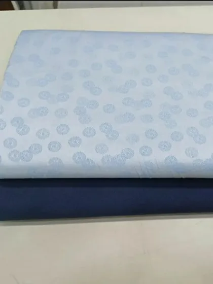 This shows a fabric combination for a client: a light blue patterned material for the shirt and a solid navy fabric for the trousers. I can help you pair fabrics for a complete outfit.