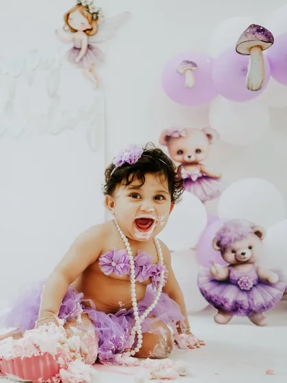 A moment of pure excitement during her purple themed cake smash. The teddy bear and fairy props add a touch of whimsy to the scene.