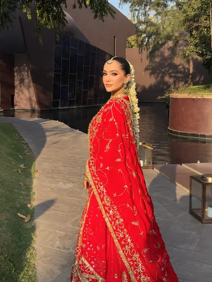 The elegance of a bride looking over her shoulder. This pose highlights the beautiful drape of the red dupatta and the intricate gold work on the lehenga.