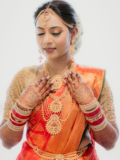 A close-up of the bride's hands, adorned with henna and bangles, as she adjusts her necklace. We love capturing these detailed shots of bridal preparations.