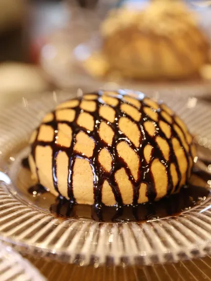 A beautiful dome-shaped dessert with a chocolate lattice drizzle, presented on a crystal plate. A simple yet elegant creation.