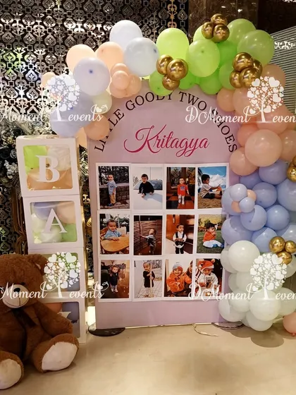 "Little Goody Two Shoes" milestone board for a second birthday, framed with soft pastel balloons and baby block props.