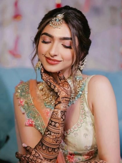 A serene portrait of a bride, her hand gently resting on her cheek, showcasing the beautiful mehndi design.