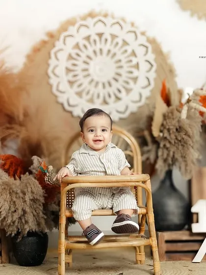 Celebrating a half birthday with a stylish boho themed sitter session. The setup features pampas grass, a rattan high chair, and a '1/2' sign to mark the milestone.