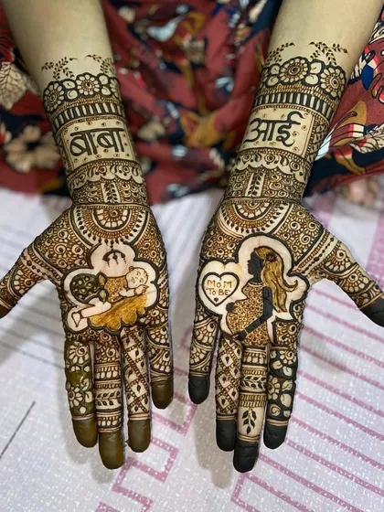 This maternity mehandi features a silhouette of a pregnant mother and a baby sleeping on a cloud, with 'आई' and 'बाबा' written above.