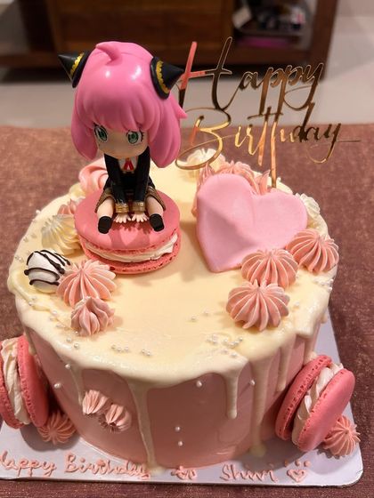 The final look of my Spy x Family anime cake, with an Anya Forger figurine sitting on a macaron. The cake itself is a chocolate sponge with pink buttercream and a white chocolate drip.
