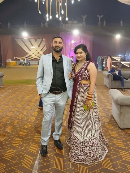A happy client posing with her partner at a wedding. She is wearing a beautiful purple lehenga with intricate floral embroidery.