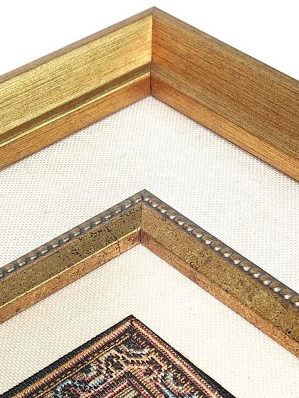 A detailed look at the corner of the framed rug, showcasing the combination of a golden fillet and a textured fabric mat. These layers add depth and a sense of luxury to the final piece.