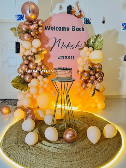 Another view of the welcome back setup, showing the cake on a modern gold stand, surrounded by balloons and lit from below.