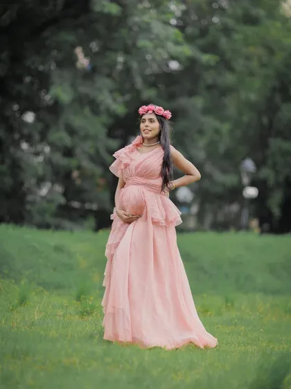 A full-length portrait in a soft pink gown. The natural park setting and the elegant pose create a serene and beautiful image.