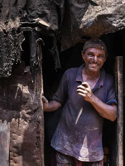 A man takes a brief pause from his work, his smile warm and genuine despite the grime. This image is a candid portrait of the human element behind the industry of Dharavi.