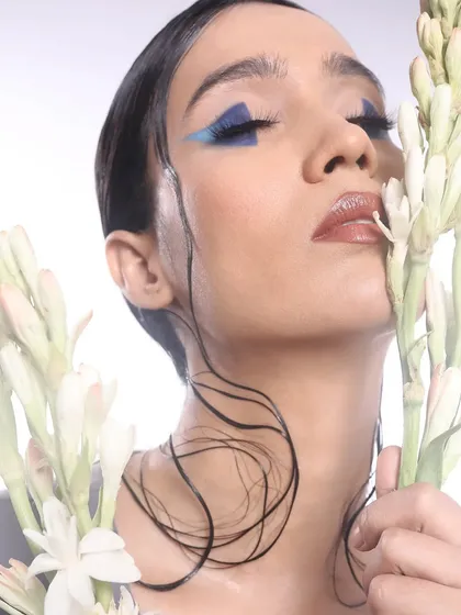 A beautiful portrait where the model's pose and the floral props enhance the artistic feel of the geometric blue eye makeup.