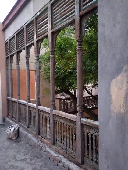 A restored wooden balcony overlooking the courtyard, its intricate jali work repaired to its former glory.