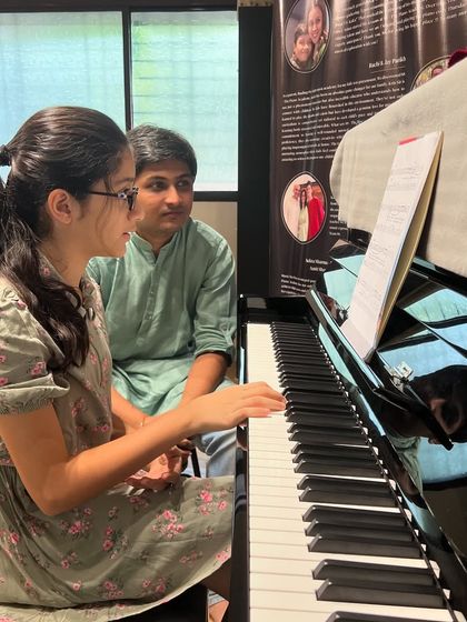A student practices piano with her teacher, both dressed in festive attire for Diwali. We celebrate all festivals with music and joy at the academy.