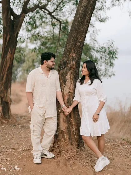 Leaning against a tree, holding hands. This is a classic, romantic pose that feels natural and comfortable, perfectly capturing the couple's easy connection.