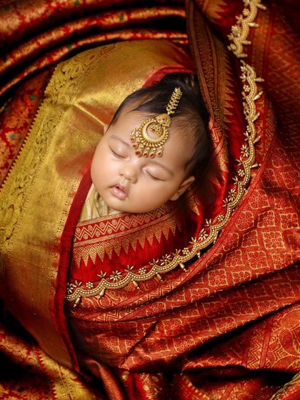 A close-up of a sleeping newborn adorned with traditional Indian jewelry, nestled within a rich, red silk saree. This is a beautiful way to incorporate family heritage into your baby's first photos.